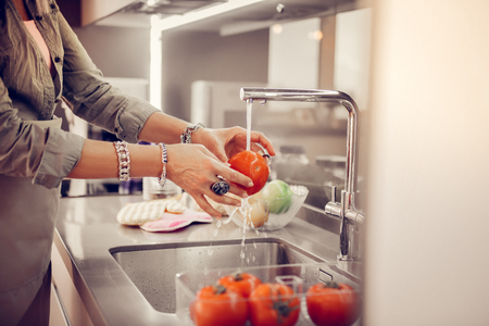 Everything must be clean. Pleasant senior woman washing tomatoes in the sink while preparing to cookの写真素材