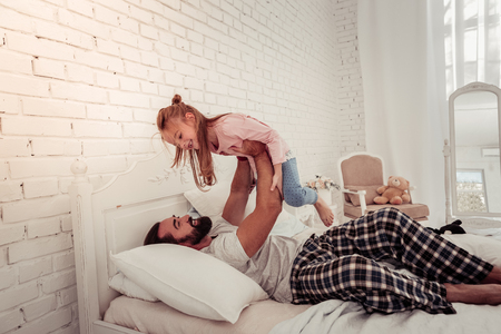 Joyful moments. Cheerful nice man looking at his daughter while holding her on his handsの写真素材