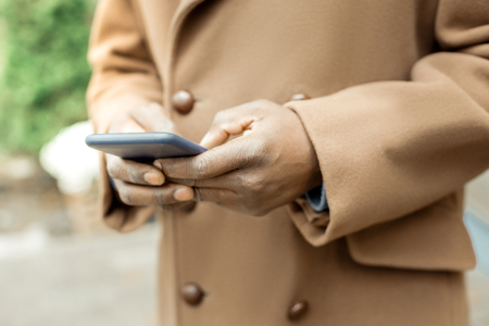 Dark smartphone. Close up of mature businessman wearing beige coat holding his dark smartphone