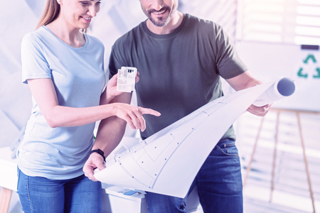 Pointing at graphic. Smiling enthusiastic architect standing next to her reliable colleague and pointing to the blueprint in his handsの写真素材