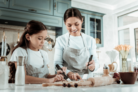 Family issues. Attentive motivated woman and kid smiling while cooking biscuits togetherの写真素材