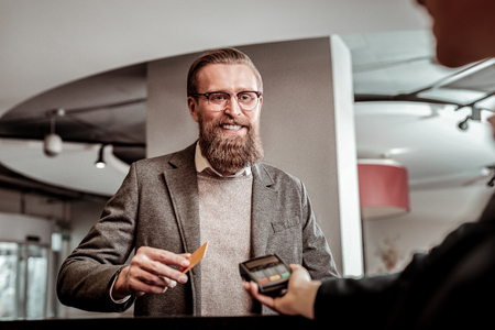 Want to pay. Cheerful young man keeping smile on his face while talking to hotel manager