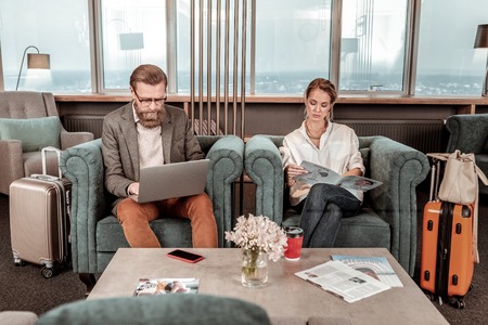 Join us. Concentrated female person crossing legs while sitting on armchair and reading articleの写真素材