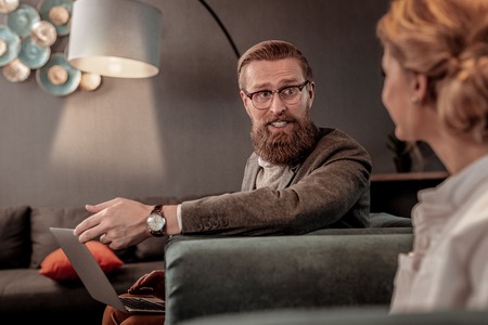 Have a look. Delighted bearded man keeping smile on his face while looking at his colleagueの写真素材