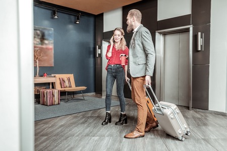 Very busy. Cheerful blonde holding her suitcase while talking per telephoneの写真素材