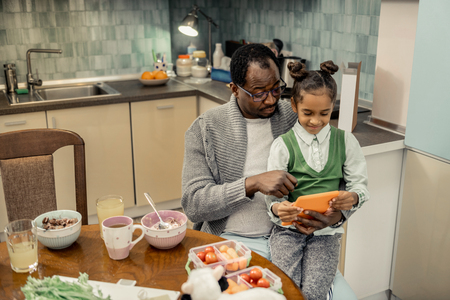 Sitting on knees. Cute stylish daughter sitting on knees of her father after eating breakfastの写真素材