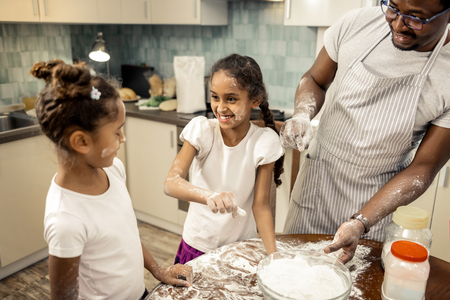 Involved in cooking. Cute little dark-haired daughters feeling amazing and involved in cooking pie