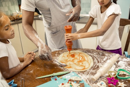 Pizza for lunch. Two cute daughters helping their loving caring father cooking pizza for lunch