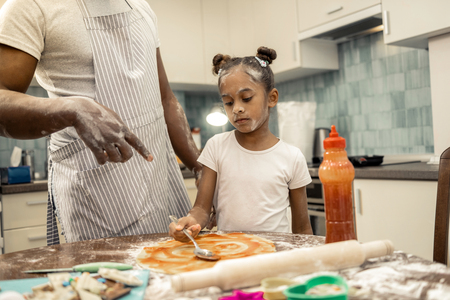 Making pizza. Father wearing striped apron teaching his little beautiful girl making pizzaの写真素材