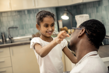 Playing tricks. Cute dark-eyed daughter playing tricks with her loving father while cooking togetherの写真素材