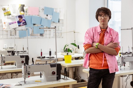 Sewing machines. Young male asian stylist wearing a pink shirt standing near sewing machinesの写真素材