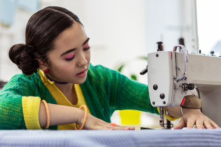 Busy day. Pretty brunette asian dressmaker wearing a pin pillow on her hand working in a studioの写真素材