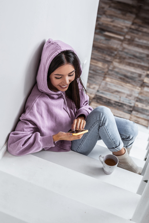 Woman in hoodie. Top view of young stylish dark-haired woman wearing purple hoodie sitting on stairsの写真素材