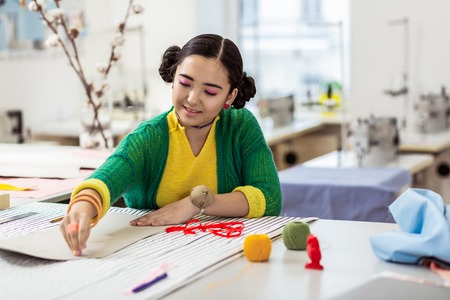 Smiling girl. Pretty brunette asian dressmaker with pink eyeshadows smiling pleasantly while working...
