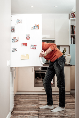 Hungry husband. Hungry husband wearing jeans opening refrigerator after coming home from workの写真素材