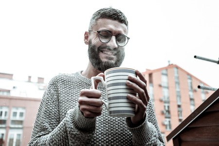Hot coffee. Delighted happy man looking into his cup while wanting to drink his coffeeの写真素材
