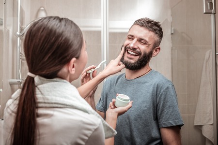 Caring girlfriend. Nice pleasant woman standing in front of her boyfriend while putting cream on his...