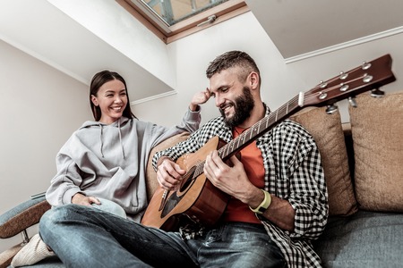 Positive young couple playing music relaxing at home togetherの写真素材