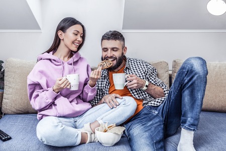 Wonderful taste. Joyful nice man trying a chocolate cookie while sitting together with his girlfriendの写真素材