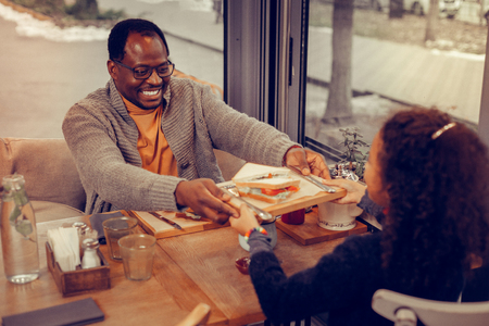 Plate with sandwich. Father wearing glasses giving wooden plate with sandwich to his cute daughterの写真素材