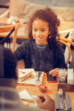 Beautiful appealing curly daughter eating sandwich sitting in cafeteria with parentsの写真素材
