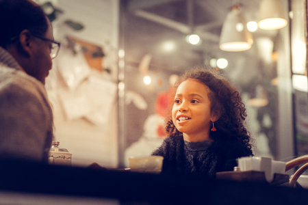 Curly dark-eyed beautiful girl wearing nice red earrings talking to her fatherの写真素材