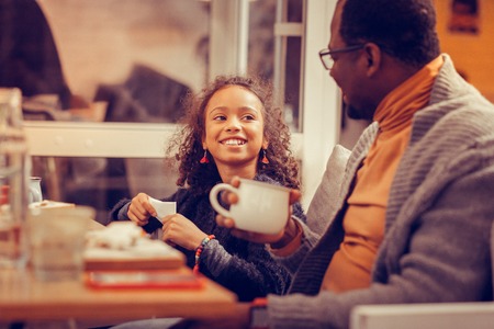 Looking at father. Happy cheerful curly girl looking at her father while eating breakfastの写真素材