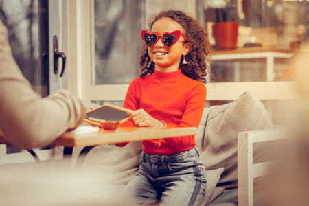 Little stylish girl wearing jeans and red polo neck wearing red heart-shaped glassesの写真素材