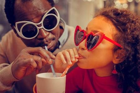 Wearing funny sunglasses. Close up of father and daughter wearing funny sunglasses drinking...
