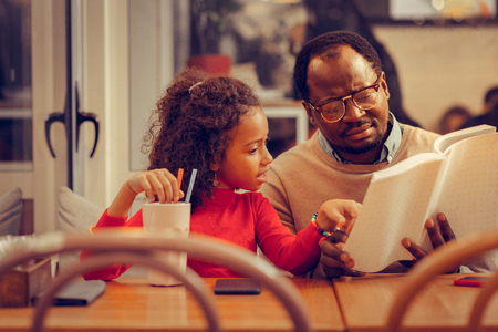 Listening attentively. Curly appealing daughter listening to her father reading book attentivelyの写真素材