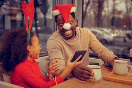 Father laughing. Father laughing while looking at Christmas photo with his cute curly daughterの写真素材