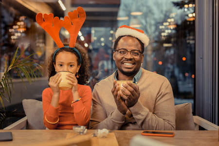 Christmas day. Father and daughter sitting at table in cafeteria on Christmas day and drinking cocoaの写真素材