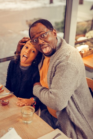 Father and daughter making funny faces while having breakfast in cafeteria togetherの写真素材