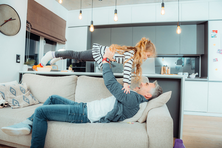 Handsome grey-haired father wearing sportswear playing with his small daughterの写真素材
