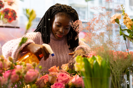 Love my job. Cute dark-skinned girl looking downwards while watering flowersの写真素材
