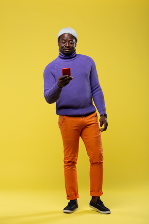 News review. Handsome dark-skinned male person standing over yellow background and reading messageの写真素材