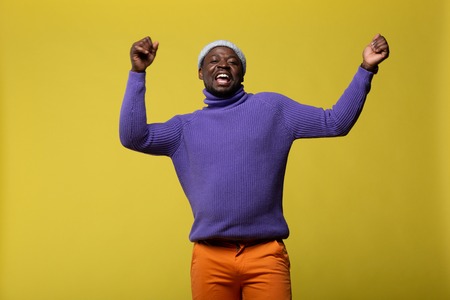 Delighted international male keeping smile on his face and raising both arms