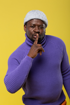 Attentive man standing over yellow background and demonstrating colorful clothesの写真素材