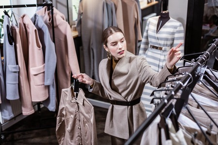 Shirts. Young long-haired pretty woman wearing big earrings choosing trendy shirts