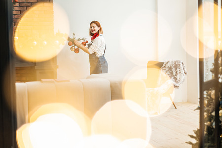 Decorating a tree. Beautiful red-haired girl wearing big earrings feeling wonderful while decorating a christmas treeの写真素材