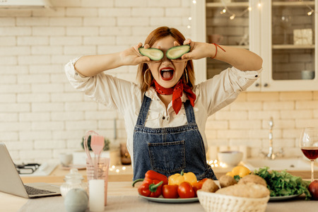 Fun in the kitchen. Cute young red-haired girl wearing a red necktie feeling funny while preparing dinnerの写真素材