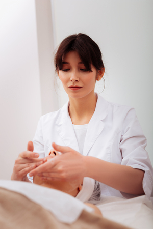Beauty therapist. Pleasant nice woman performing a special procedure while working in the beauty clinicの写真素材