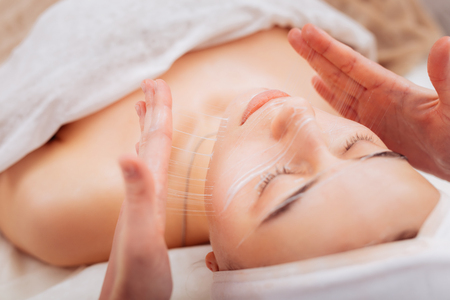 Staying beautiful. Nice pleasant woman lying on the medical bed while having a special cream applied on her skinの写真素材