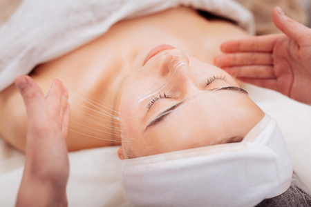 Revitalized skin. Pleasant young woman feeling relaxed while enjoying her facial procedureの写真素材