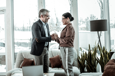 Hands. Tall grey-haired handsome man wearing a dark jacket holding hands of his partnerの写真素材