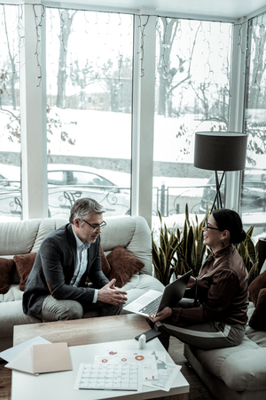 Looking at the pictures. Tall grey-haired handsome man wearing a dark jacket looking at the picture on a laptopの写真素材