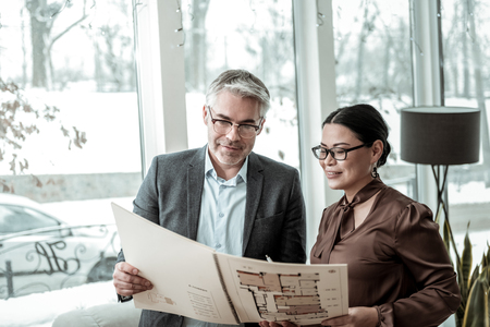 Good news. Dark-haired elegant woman wearing a brown satin blouse discussing the project with her business partnerの写真素材