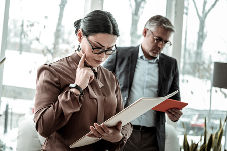 New project. Brunette adult businesswoman wearing a brown satin blouse reading information about a new projectの写真素材