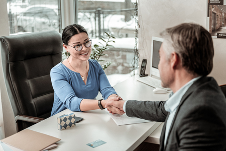 New employee. Dark-haired beautiful asian woman wearing a blue shirt shaking hands with a new employeeの写真素材