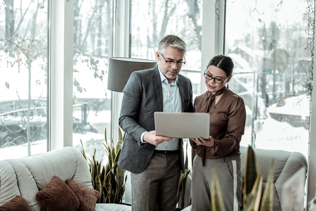 Good team. Tall grey-haired handsome man wearing a dark jacket and his partner working togetherの写真素材